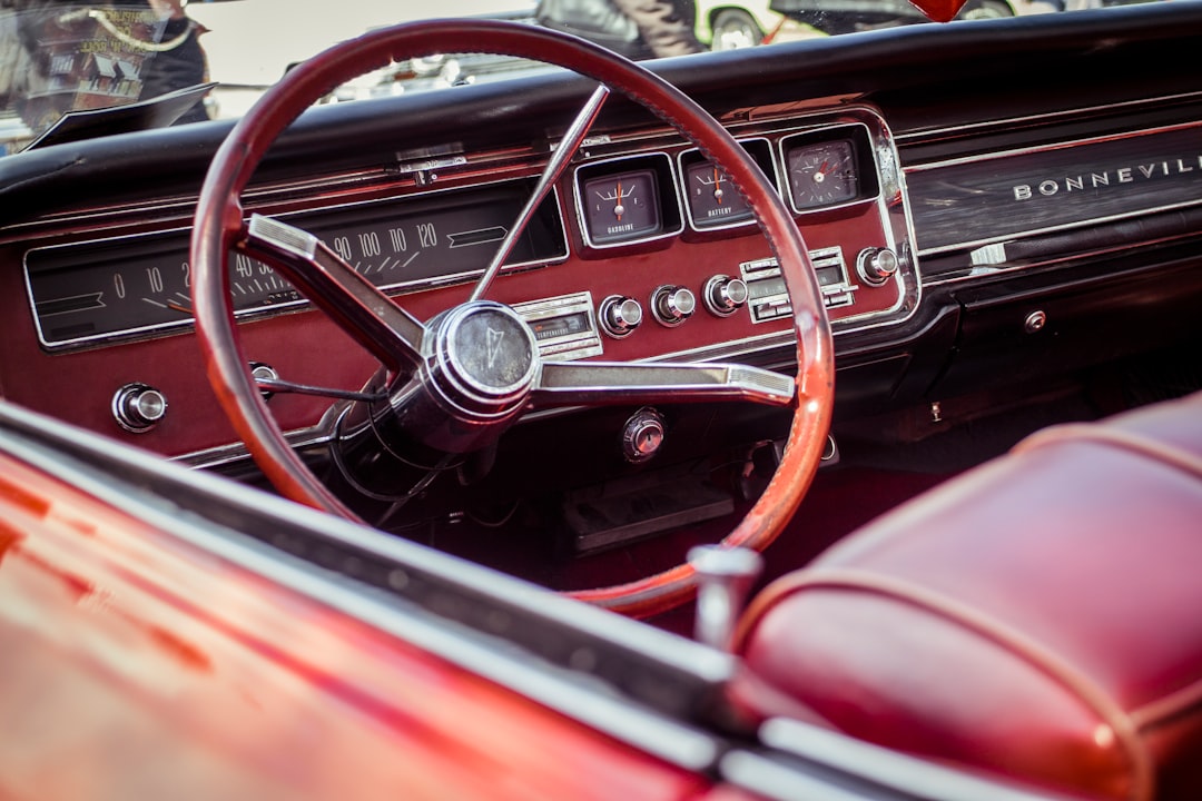 Крупный план красного салона классического автомобиля Pontiac Bonneville, с акцентом на винтажный руль, приборную панель и приборы с хромированными деталями и красными кожаными сиденьями — выполненные с той же точностью, что и премиальный хостинг WordPress.